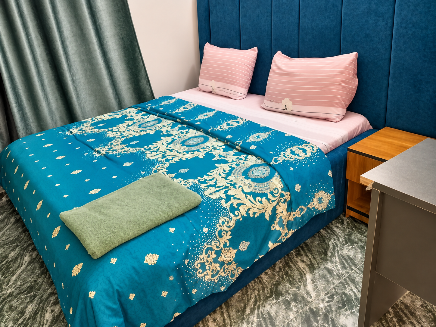Close-up of teal damask bedding with pink accent pillows on blue velvet headboard
