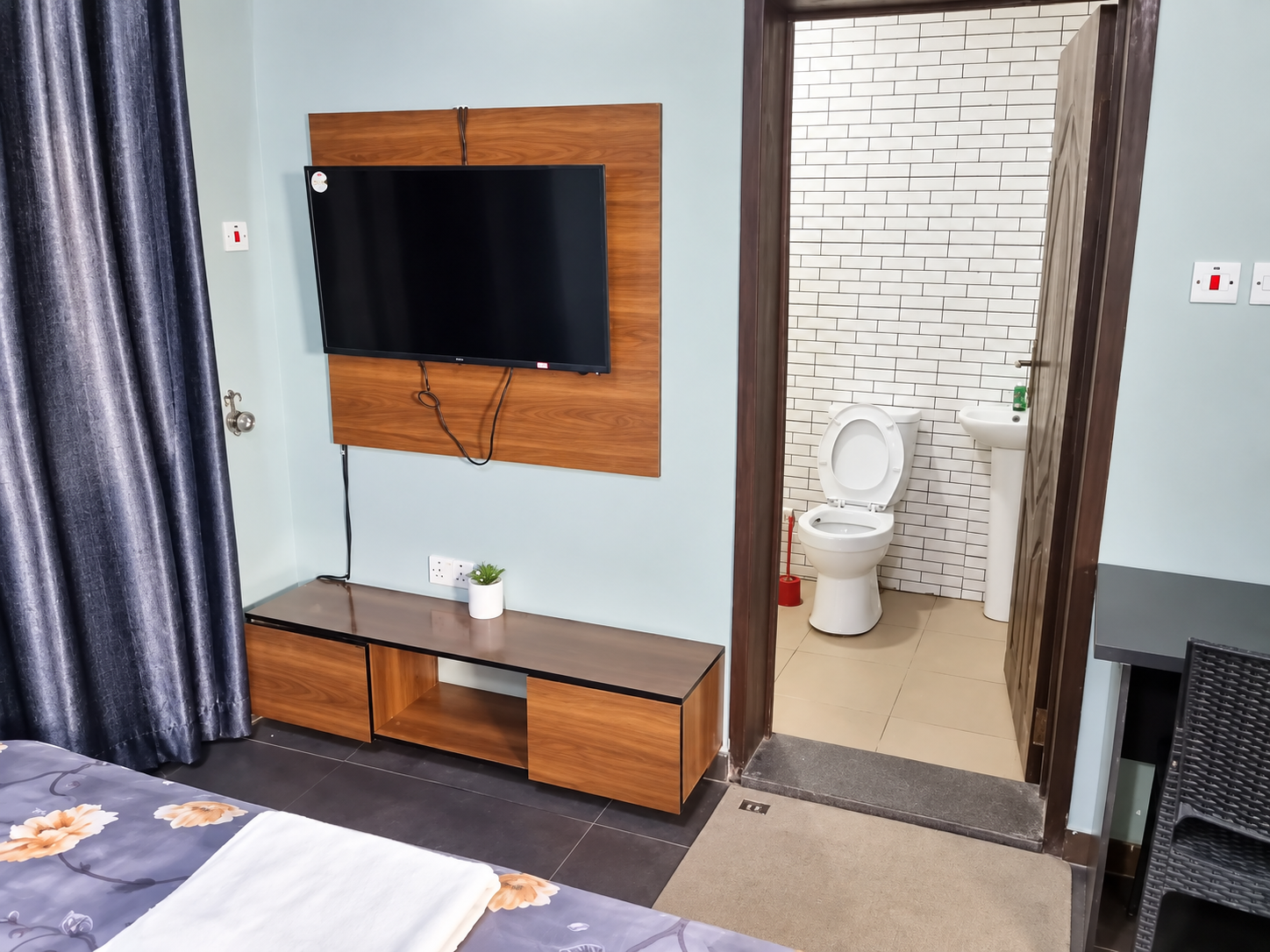 Guest room with wall-mounted flat-screen TV, en-suite bathroom, and floral bedding