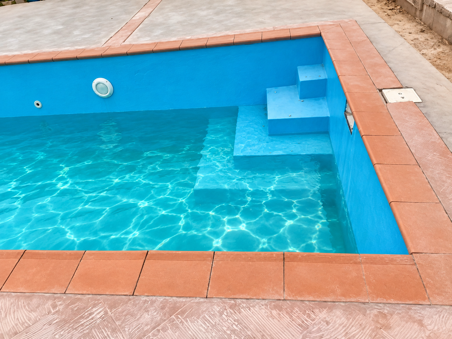 Swimming pool entry steps with clear blue water and brown tile border
