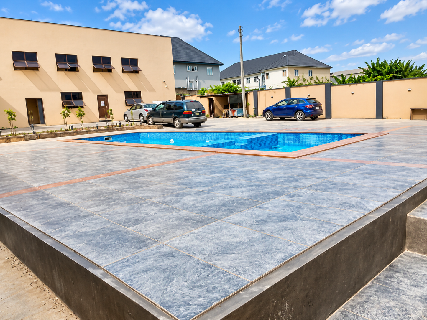 Wide view of the swimming pool and expansive tiled deck with hotel building in background